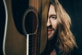 Handsome bearded long haired man holding guitar and smiling at camera