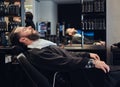 Handsome bearded male waits for the hairdresser sitting on a barber chair.