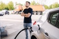 Handsome bearded man cross the arms during refueling car. Male looking on the scoreboard at gas station