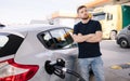 Handsome bearded man cross the arms during refueling car. Male looking on the scoreboard at gas station