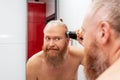 Handsome bearded man cutting his own hair with hair clipper in bathroom in front of mirror at home. Closeup Royalty Free Stock Photo