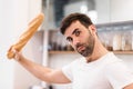 Handsome bearded man holding baguette over kitchen background at home.