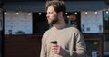 Handsome bearded man holding cup of take-out coffee and smiling standing on street on nice day, drinking coffee. Royalty Free Stock Photo