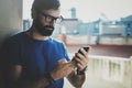 Handsome bearded man holding smartphone hands and touching screen of modern mobile phone. Blurred background.Blogger