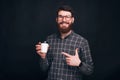 Handsome bearded man is pointing at his take away cup on black background. Royalty Free Stock Photo