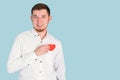 A handsome bearded man puts a red heart in the pocket of a white shirt standing on a blue background, copyspace Royalty Free Stock Photo