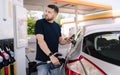 Handsome bearded man refueling car and looking on the scoreboard while standing on self service gas station