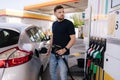 Handsome bearded man refueling car and looking on the scoreboard while standing on self service gas station