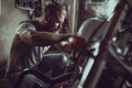 Handsome bearded man repairing his motorcycle in the garage. A man wearing jeans and a t-shirt