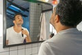 Handsome bearded man is shaving his face and neck with trimmer machine in front of bathroom mirror Royalty Free Stock Photo