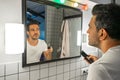 Handsome bearded man is shaving his face with trimmer machine in front of bathroom mirror Royalty Free Stock Photo