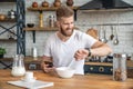 Handsome bearded man is sitting in the kitchen having breakfast cereals and milk, coffee and bananas. checking his mail on the Royalty Free Stock Photo