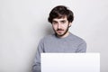 Handsome bearded man with sylish dark hair wearing casual grey sweater checking e-mail on laptop, using free wireless internet con