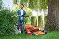 Handsome bearded man trimming lawn with electric mower, working on backyard at sunny day. Royalty Free Stock Photo