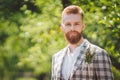 Handsome bearded man in vintage clothing. Portrait stylish groom in plaid jacket on his wedding day in the park. Rustic hipster