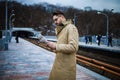 Young bearded man reads the latest news. Confident young man in winter coat reading newspaper while standing outdoors on bridge Royalty Free Stock Photo