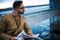 Young bearded man reads the latest news. Confident young man in winter coat reading newspaper while standing outdoors on bridge