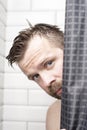 Handsome, bearded man with wet hair looks from behind a curtain