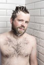 A bearded man in a white foam from the shampoo standing in the s