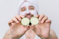 Handsome bearded man in white towel having white mask on his face and posing with slices of fresh cucumber, showing it Royalty Free Stock Photo