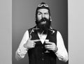 Handsome bearded pilot or aviator man with long beard and mustache on funny face holding glass of alcoholic shot in Royalty Free Stock Photo