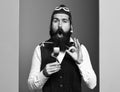 Handsome bearded pilot or aviator man with long beard and mustache on funny face holding glass of alcoholic shot in Royalty Free Stock Photo