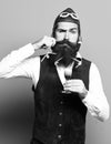 Handsome bearded pilot or aviator man with long beard and mustache on funny face holding glass of alcoholic shot in Royalty Free Stock Photo