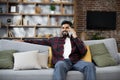 Handsome bearded positive man sitting on couch and calling to his friend using smartphone indoors. Royalty Free Stock Photo