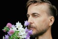 Handsome bearded stylish man sniffs aroma of tender wild flowers on black background. Gift for my love. Feeling nature