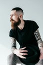 handsome bearded tattooed man holding hat and looking away