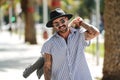 Handsome bearded and tattooed man wearing fashionable shirt, sunglasses and black hat posing on the city street Royalty Free Stock Photo