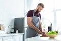 handsome bearded young man in apron cutting vegetables while cooking Royalty Free Stock Photo