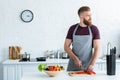 handsome bearded young man in apron looking away while cooking Royalty Free Stock Photo