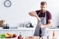 handsome bearded young man in apron opening bottle of wine and looking at camera while cooking Royalty Free Stock Photo