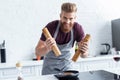 handsome bearded young man in apron smiling at camera while cooking delicious beef steak Royalty Free Stock Photo