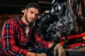 handsome bike repair station worker with wrench sitting in front of motorcycle and looking