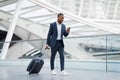 Handsome Black Businessman In Airport Walking With Suitcase And Using Smartphone Royalty Free Stock Photo