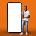 Handsome Black Guy Standing Near Huge Blank Cellphone And Pointing At It Royalty Free Stock Photo