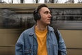 handsome black haired man in blue jeans jacket is standing on the bus stop, waiting for a bus