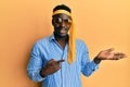 Handsome black man drunk wearing tie over head and sunglasses amazed and smiling to the camera while presenting with hand and Royalty Free Stock Photo