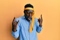 Handsome black man drunk wearing tie over head and sunglasses shouting with crazy expression doing rock symbol with hands up Royalty Free Stock Photo