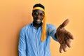 Handsome black man drunk wearing tie over head and sunglasses smiling friendly offering handshake as greeting and welcoming Royalty Free Stock Photo