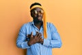 Handsome black man drunk wearing tie over head and sunglasses smiling with hands on chest with closed eyes and grateful gesture on Royalty Free Stock Photo