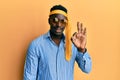 Handsome black man drunk wearing tie over head and sunglasses smiling positive doing ok sign with hand and fingers Royalty Free Stock Photo