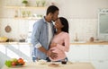 Handsome black man hugging his beautiful pregnant wife and kissing her on forehead in kitchen Royalty Free Stock Photo