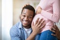 Handsome black man listening his wife`s pregnant belly at home Royalty Free Stock Photo