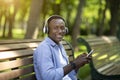 Handsome black man relaxing on bench in park and enjoying his favorite music on smartphone Royalty Free Stock Photo