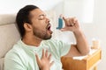 Handsome black man sitting alone at home, using asthma pump Royalty Free Stock Photo