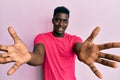 Handsome black man wearing casual pink t shirt looking at the camera smiling with open arms for hug Royalty Free Stock Photo