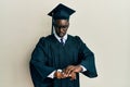 Handsome black man wearing graduation cap and ceremony robe checking the time on wrist watch, relaxed and confident Royalty Free Stock Photo